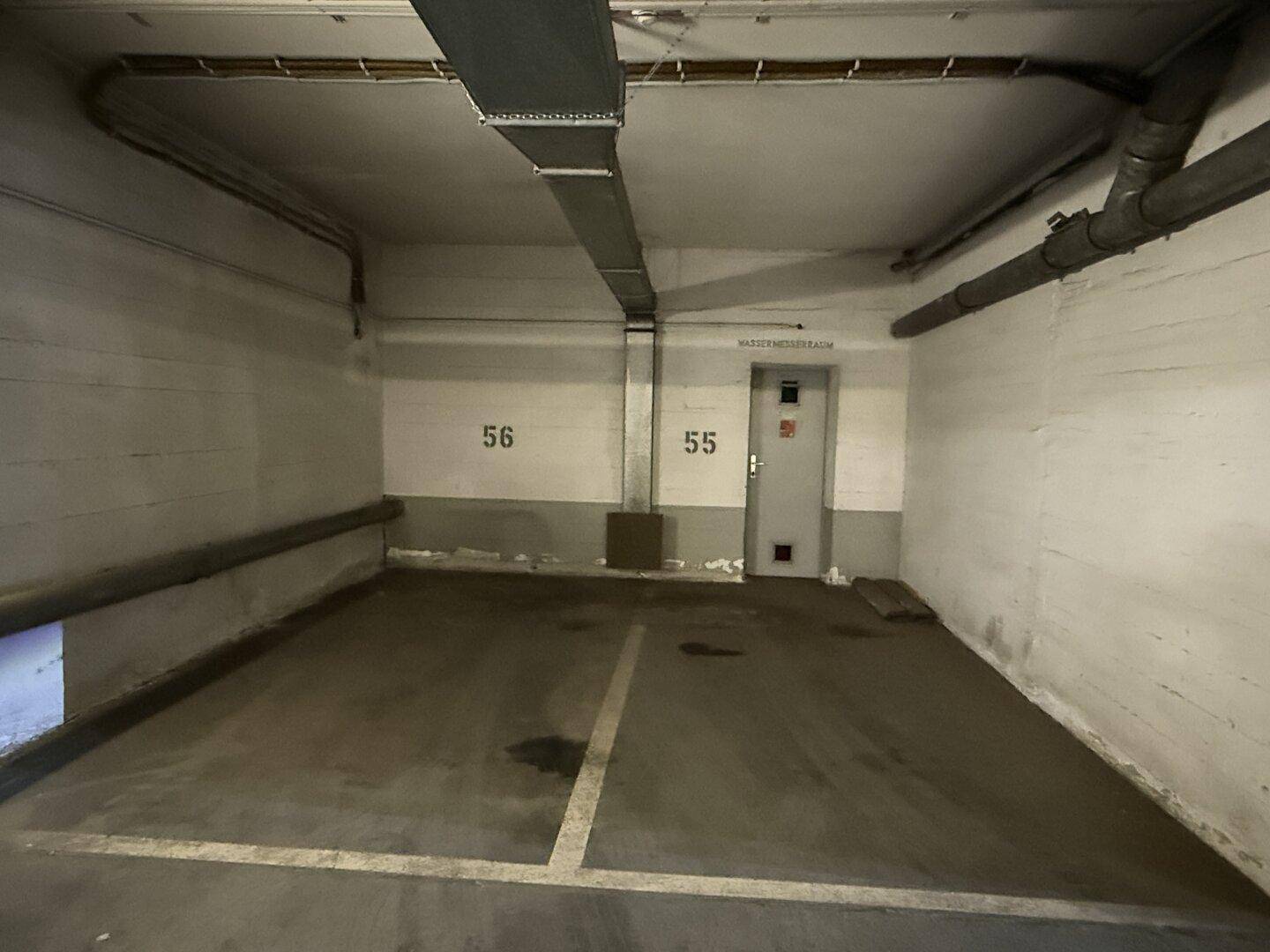 Einzelner Parkplatz in einer Tiefgarage mit Betonwänden, gekennzeichnet mit Nummer 56, neben einer Tür.