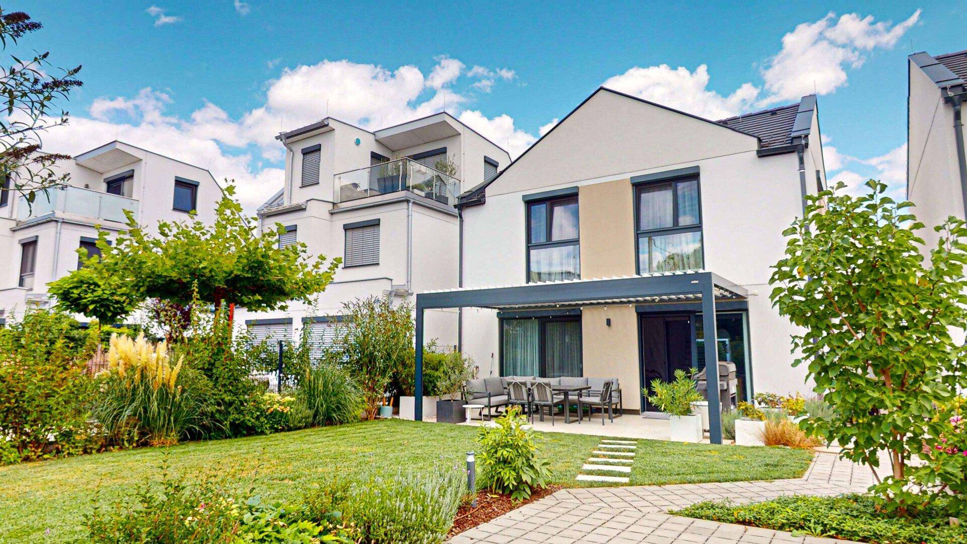 Attraktives Reihenhaus mit gepflegtem Garten, großer Terrasse und moderner Pergola unter blauem Himmel.