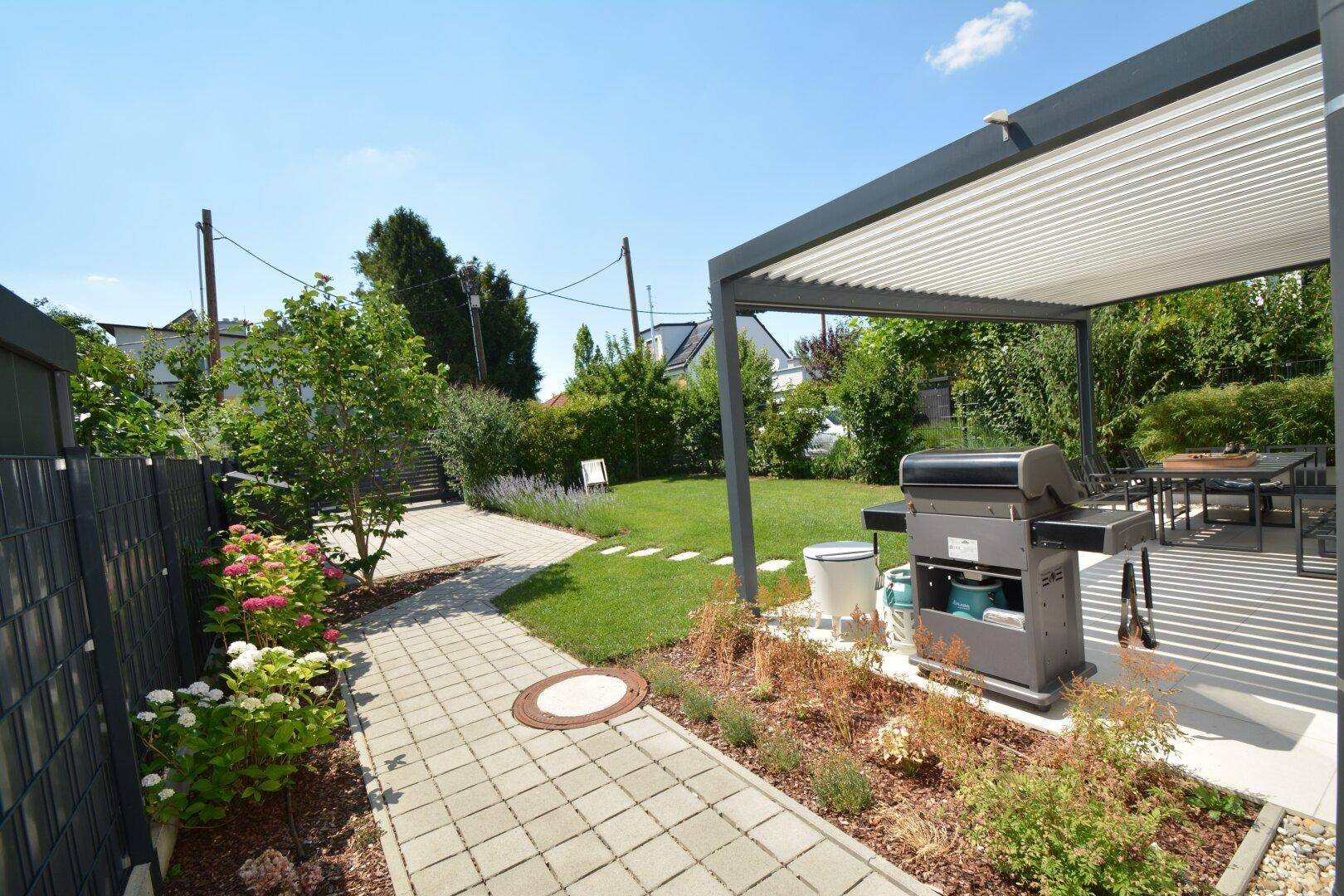 Gepflegter Gartenbereich mit Grillplatz unter einer modernen Pergola und Sitzgelegenheiten im Freien.