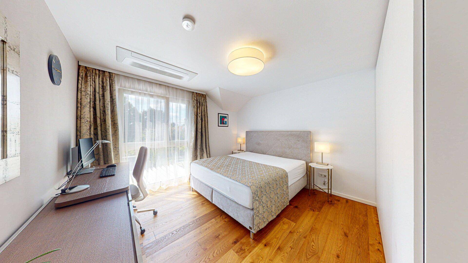 Helles Schlafzimmer mit Holzboden, großem Bett, Schreibtisch und Klimaanlage für Komfort.