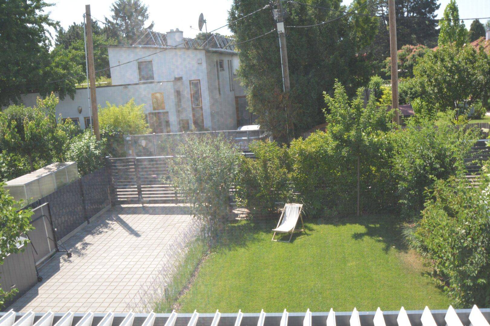 Blick von oben auf einen grünen Garten mit Liegestuhl und gepflasterter Einfahrt.