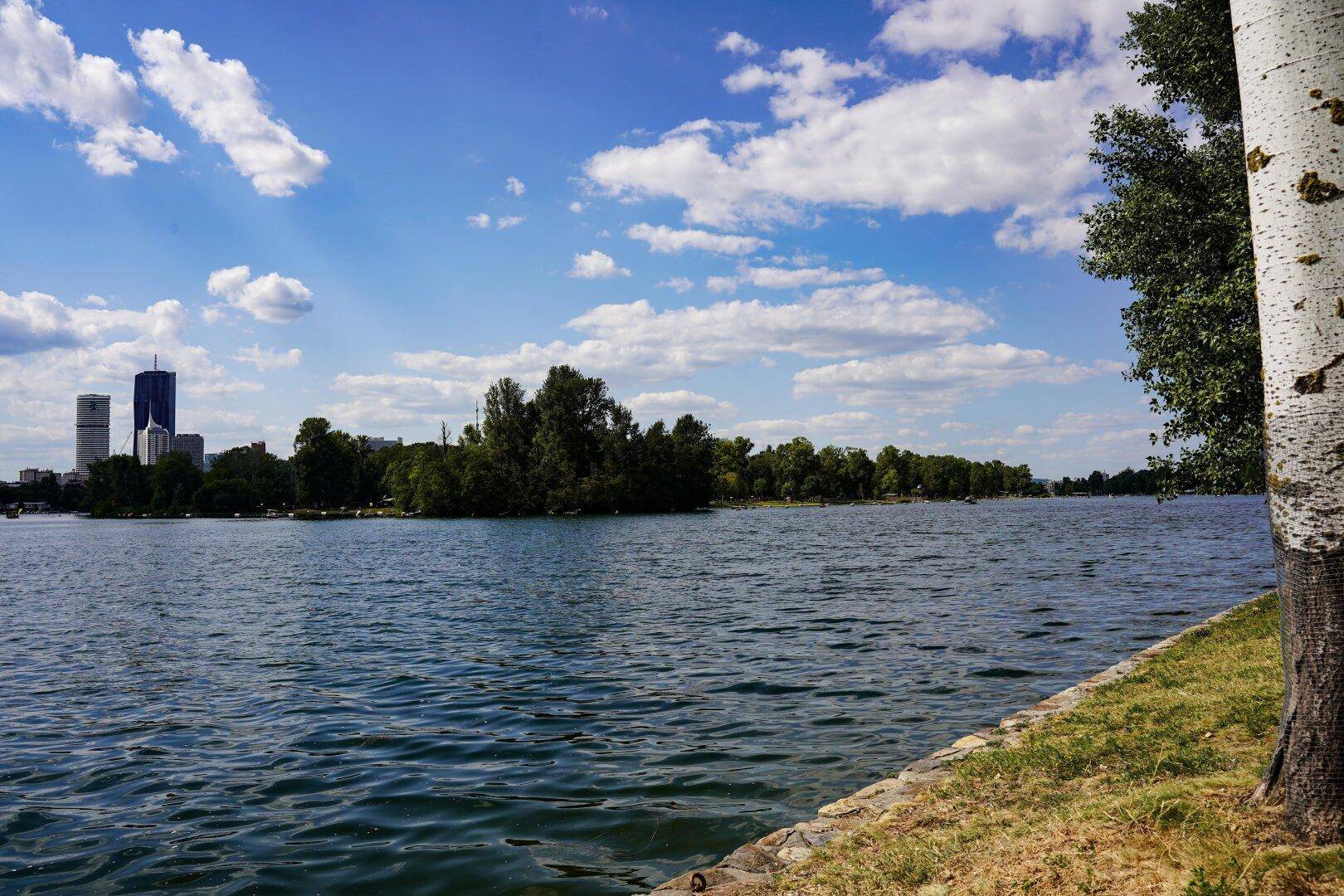 Weiter Blick über einen See mit Stadtpanorama und blauem Himmel an einem sonnigen Tag.