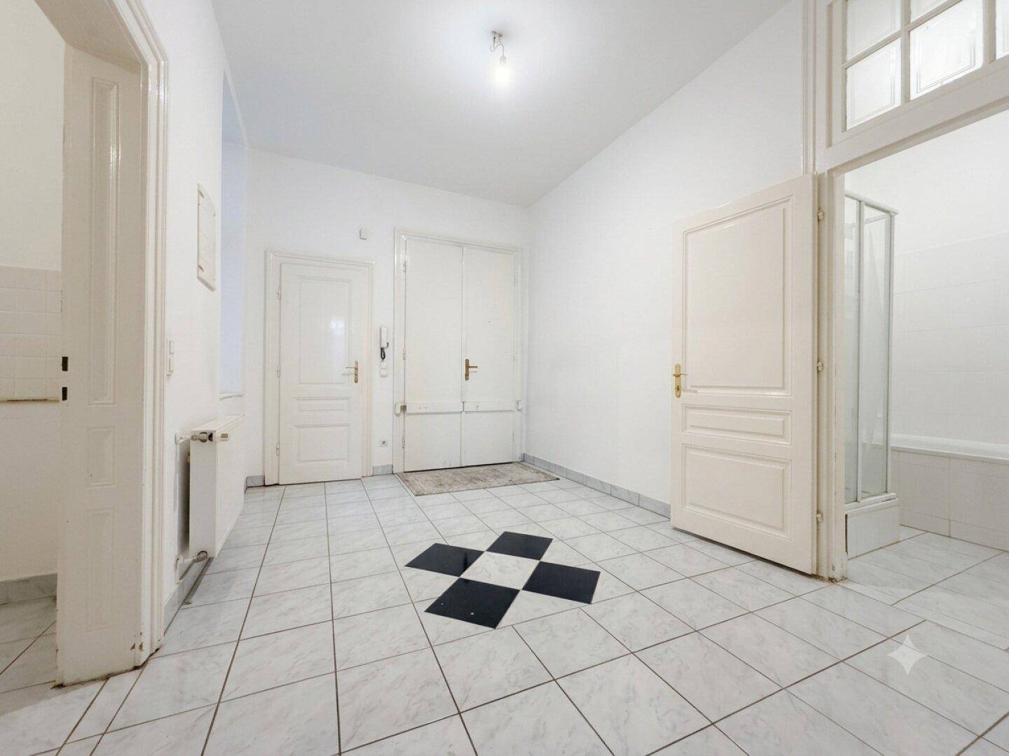 Heller Flur mit weiß-schwarz gefliestem Boden und Zugang zu verschiedenen Räumen, inklusive Badezimmer.
