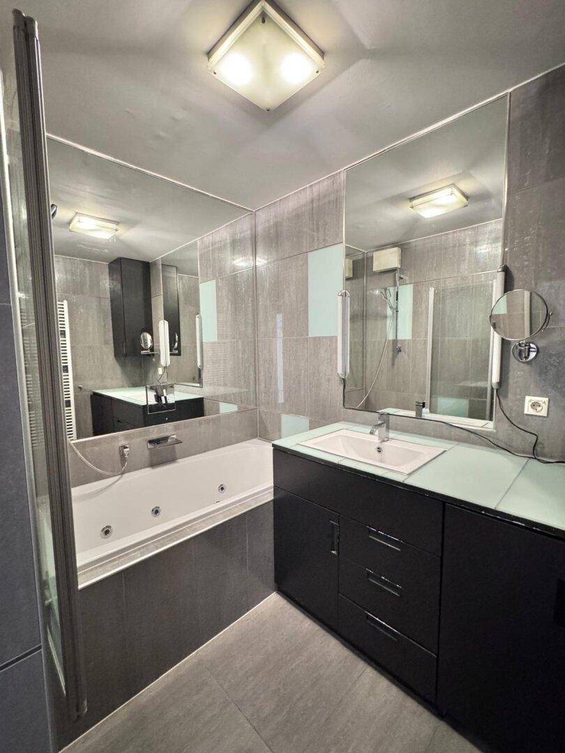 Modernes Badezimmer mit Whirlpool-Badewanne, großem Spiegel und dunklen Fliesen.