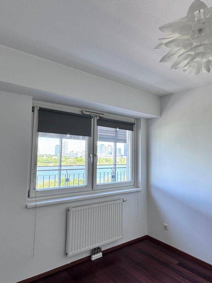 Helles Schlafzimmer mit Fenster, Heizkörper und Blick auf die Stadt und den Fluss.