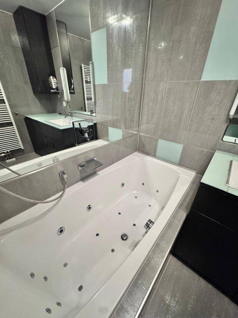 Whirlpool-Badewanne in einem modern gefliesten Badezimmer mit Spiegelwand.