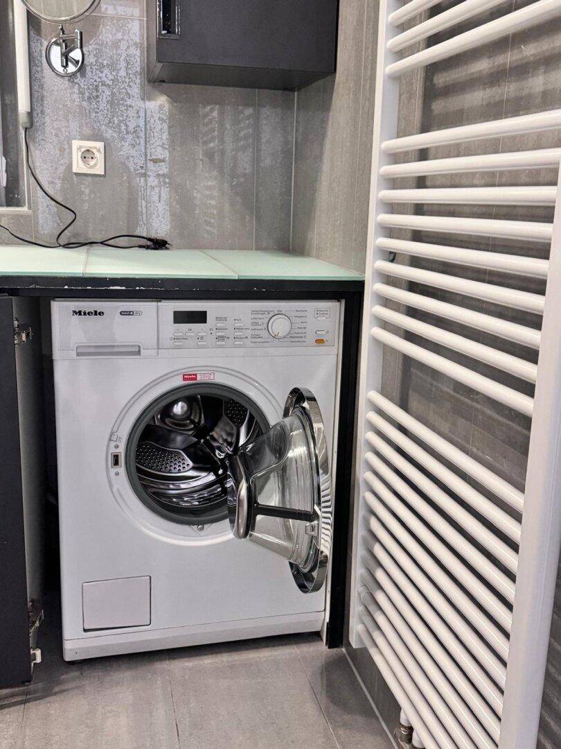 Waschmaschine von Miele und beheizter Handtuchhalter in einem modernen Badezimmer.