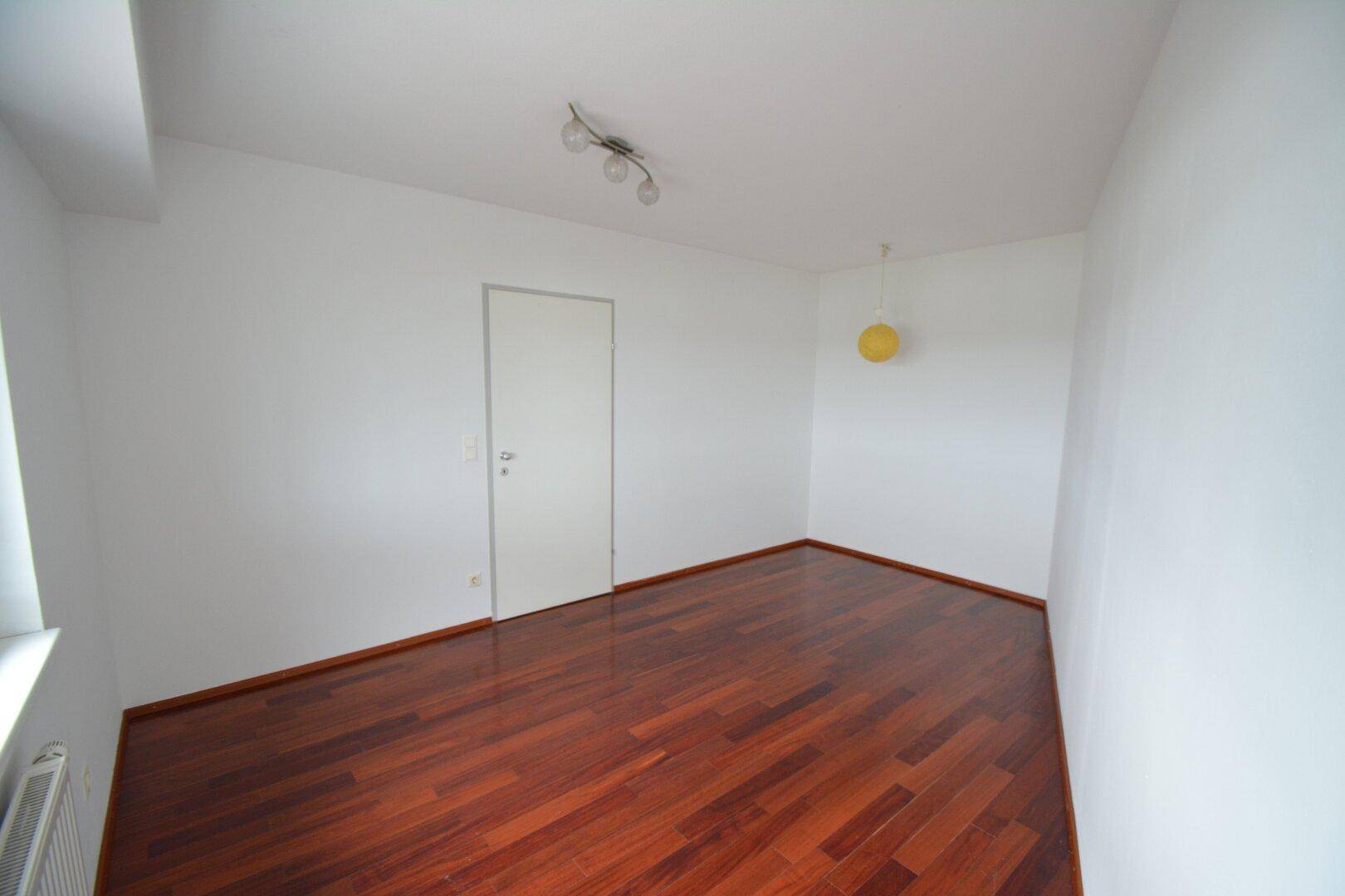 Leeres Zimmer mit Parkettboden und weiß gestrichenen Wänden, bereit zur individuellen Gestaltung.