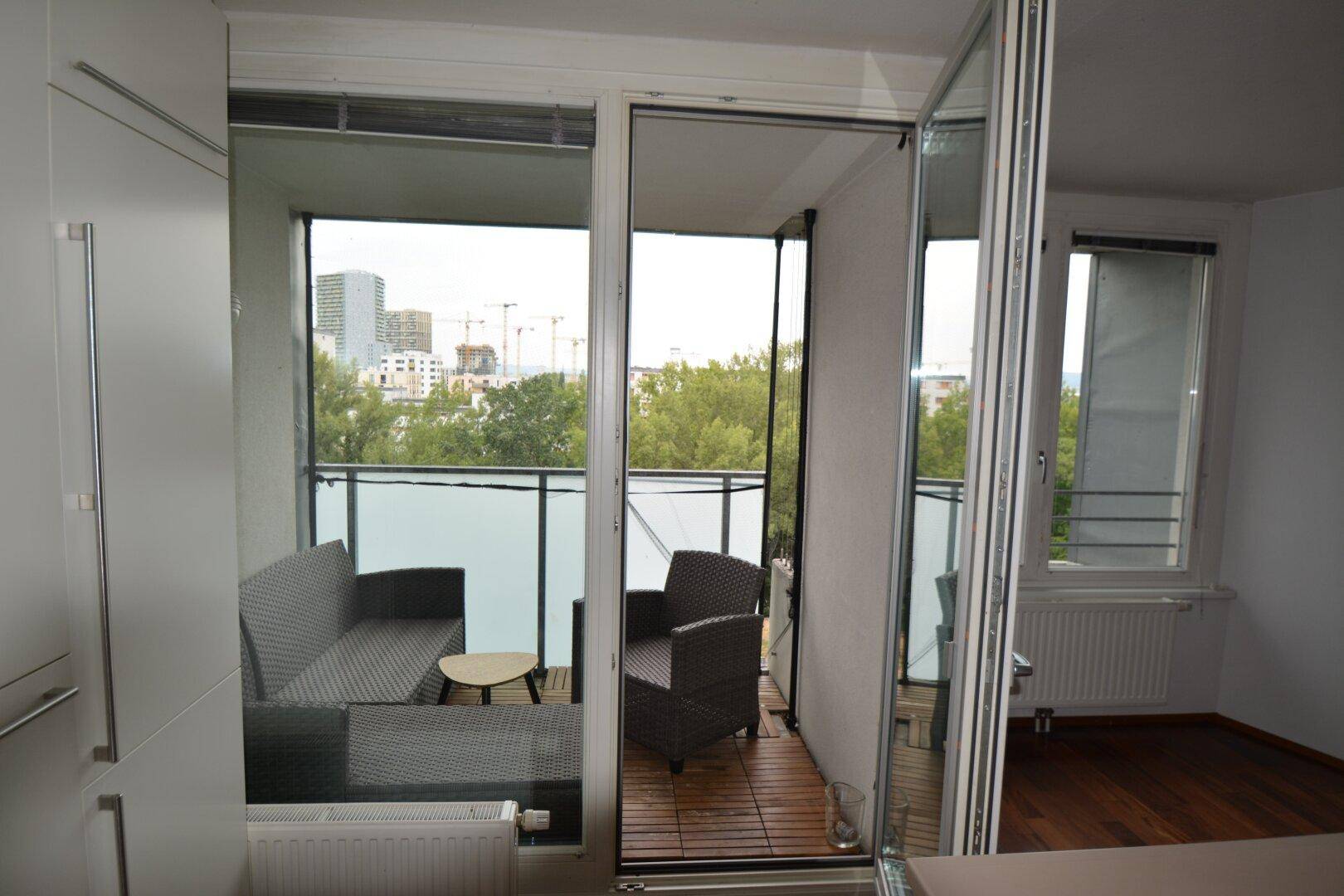 Blick von der Küche auf den möblierten Balkon mit Stadtblick und viel Grün.