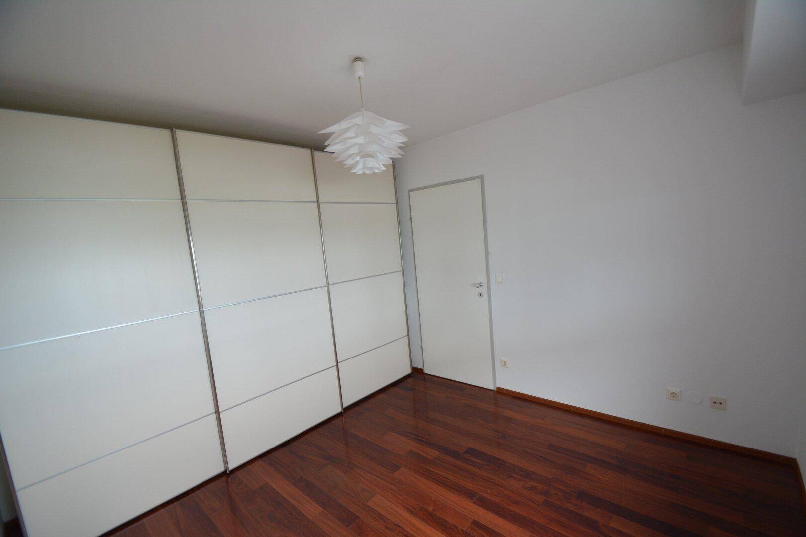 Schlafzimmer mit großem weißen Einbauschrank und dunklem Holzparkett.