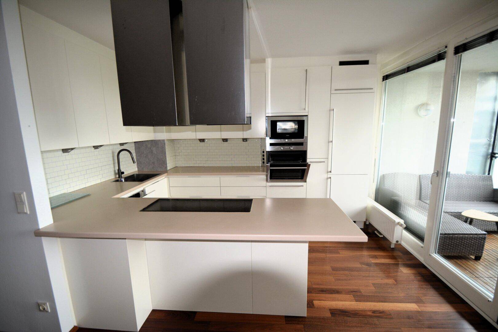 Moderne Einbauküche mit weißen Schränken, Kochinsel und Zugang zum Balkon.