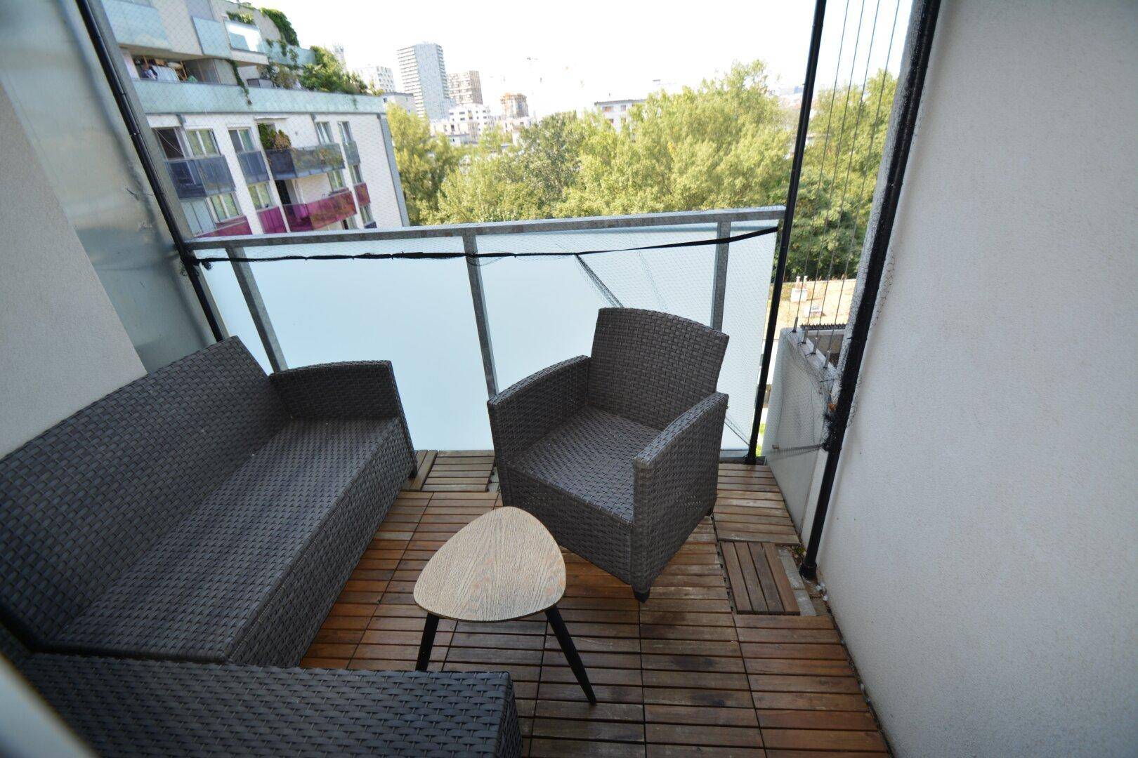 Gemütlicher Balkon mit Rattanmöbeln und Blick auf die umliegende Stadtbegrünung.