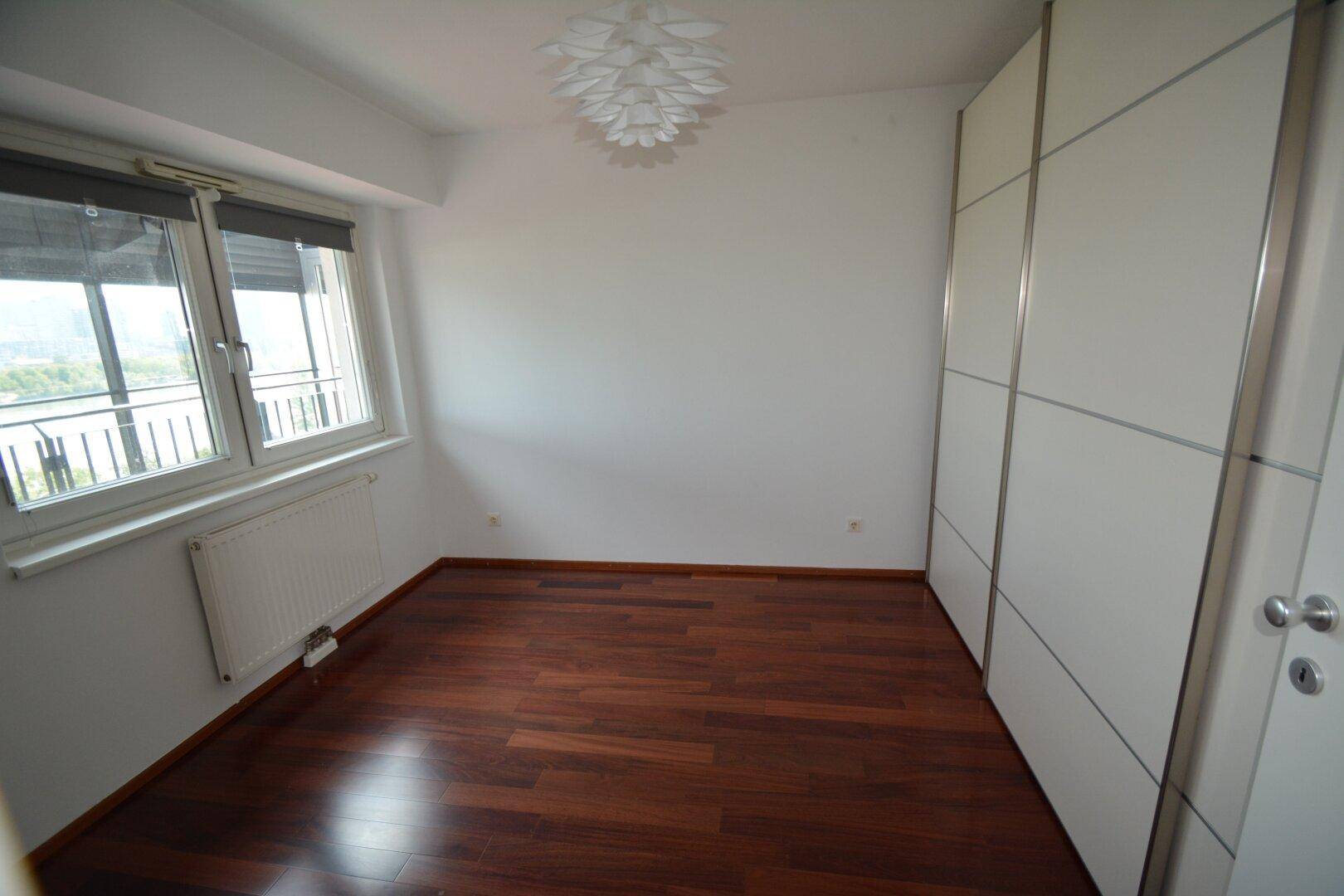 Helles Schlafzimmer mit Parkettboden, Einbauschrank und Fenster mit Ausblick.