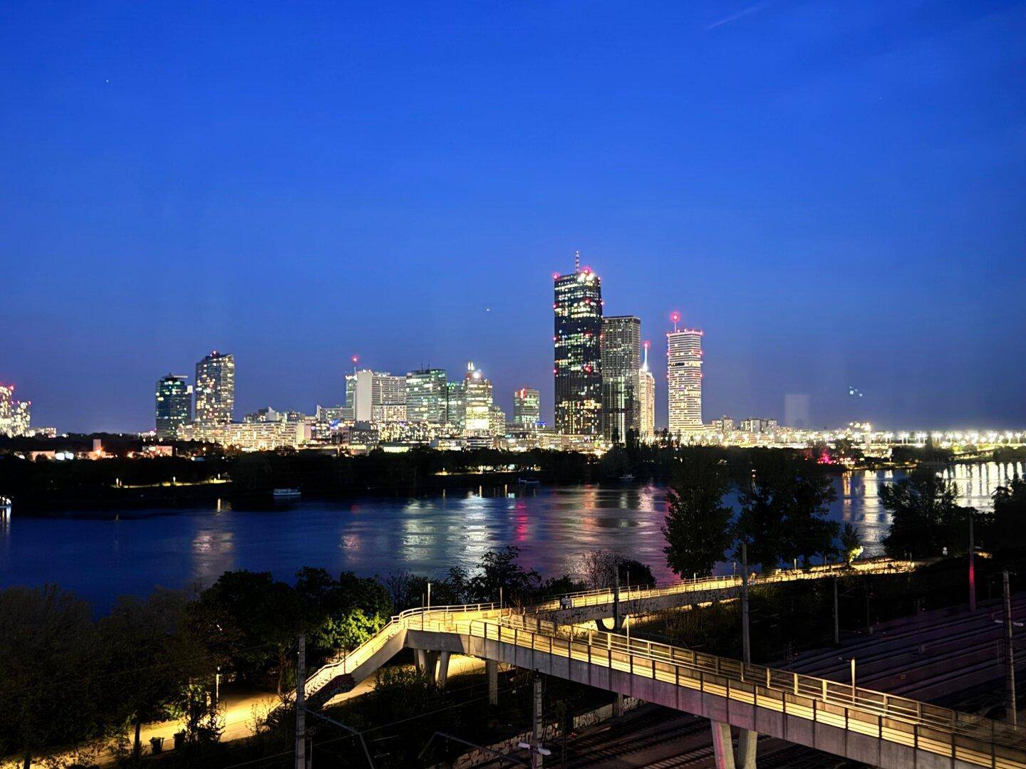 Beeindruckender nächtlicher Blick auf die beleuchtete Stadt-Skyline und den Fluss mit Brücke.