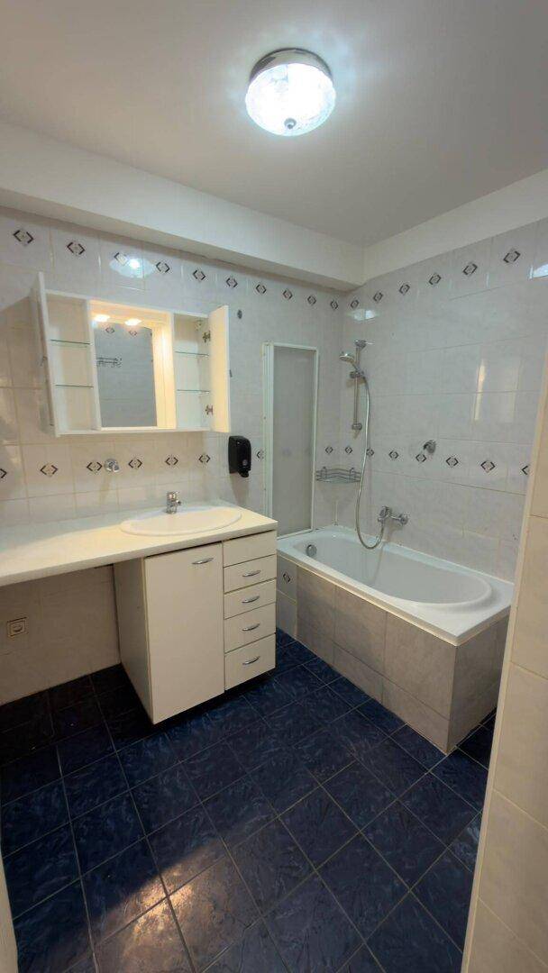 Badezimmer mit Badewanne, Waschbecken und Spiegelschrank, gefliest in Blau und Weiß.