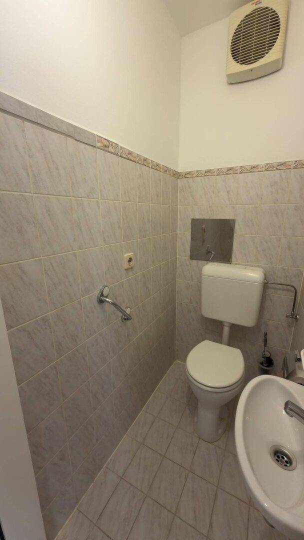 Kleines Gäste-WC mit Toilette, Waschbecken und Wandfliesen in hellem Design.