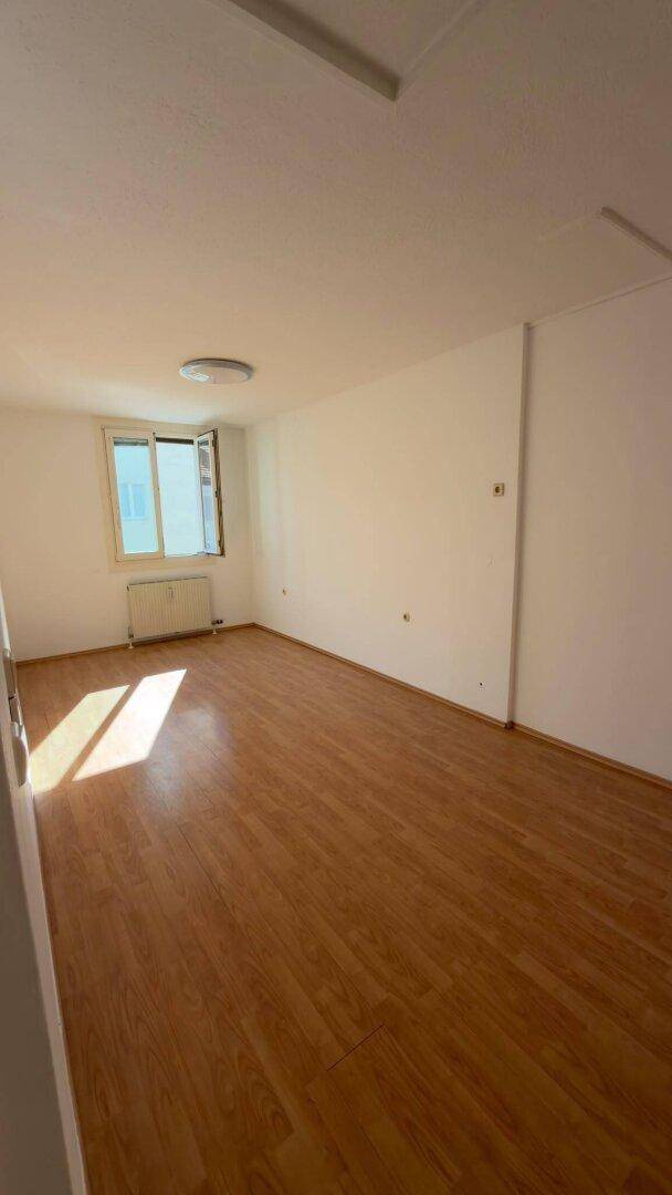 Geräumiges, helles Zimmer mit Holzboden und einem Fenster, ideal als Schlafzimmer.