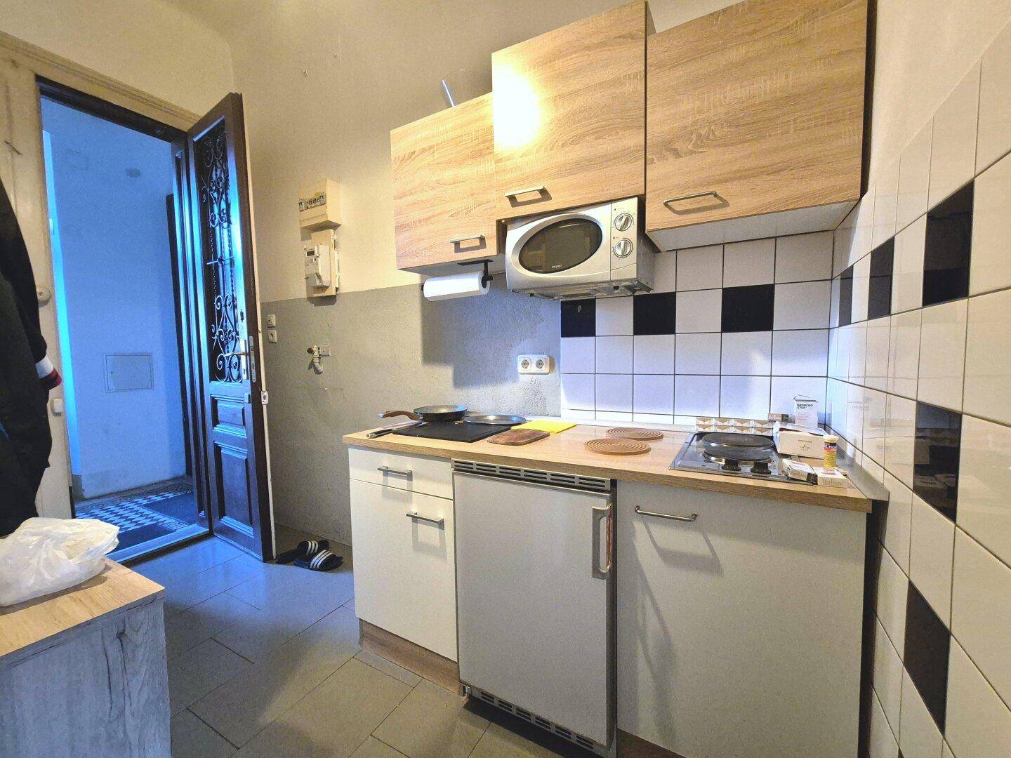 Kleine Küchenzeile mit Holzschränken, Mikrowelle und Kühlschrank, ideal für kompaktes Wohnen.