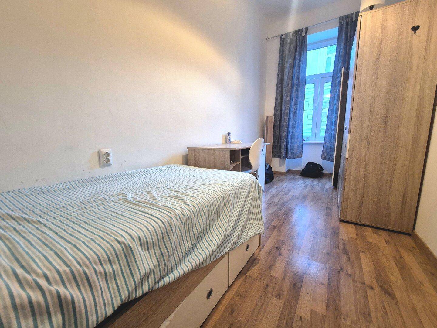 Helles Schlafzimmer mit Einzelbett, Schreibtisch und Kleiderschrank, ausgestattet mit Laminatboden.