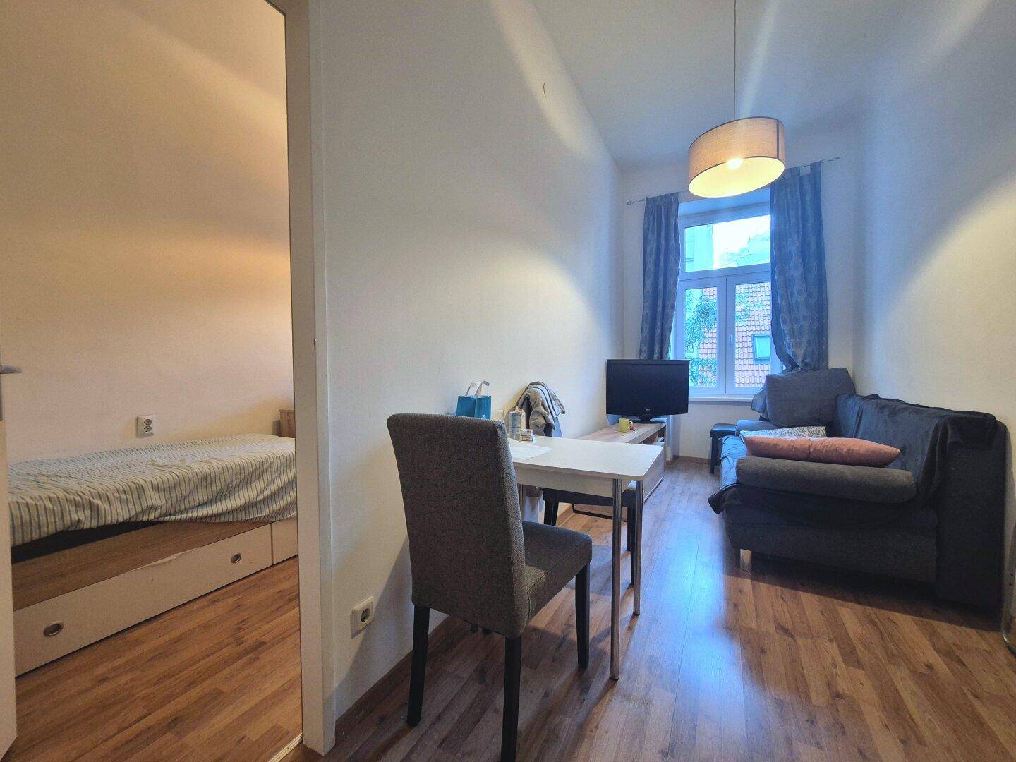 Gemütlicher Wohnbereich mit Sofa, kleinem Esstisch und Blick in ein angrenzendes Schlafzimmer.