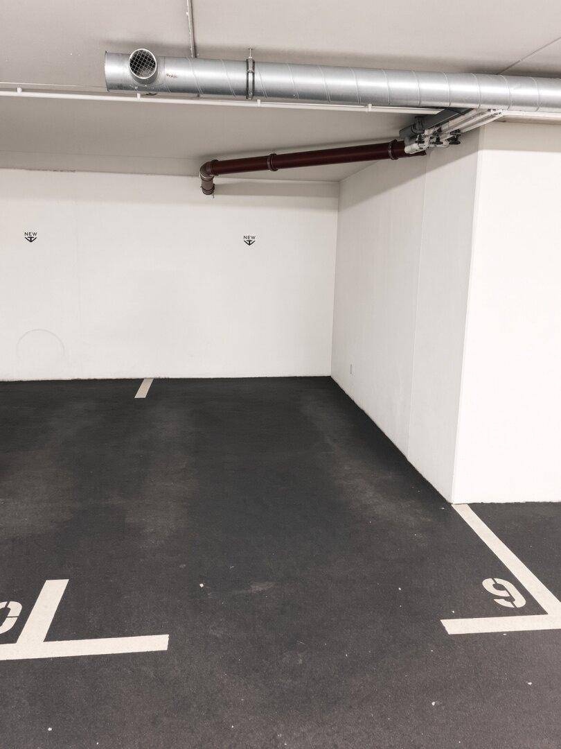 Leerer Parkplatz in einer Tiefgarage mit sichtbaren Leitungen an der Decke.