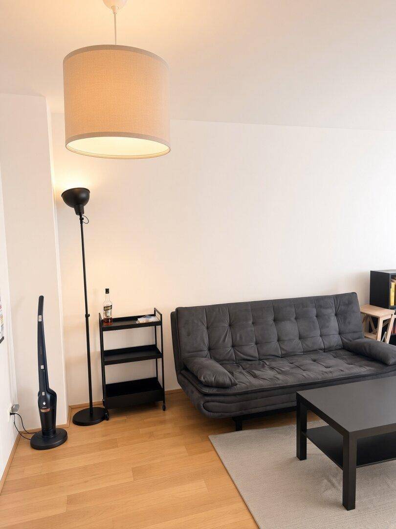 Gemütliches Wohnzimmer mit dunklem Sofa, Couchtisch und Stehlampe.