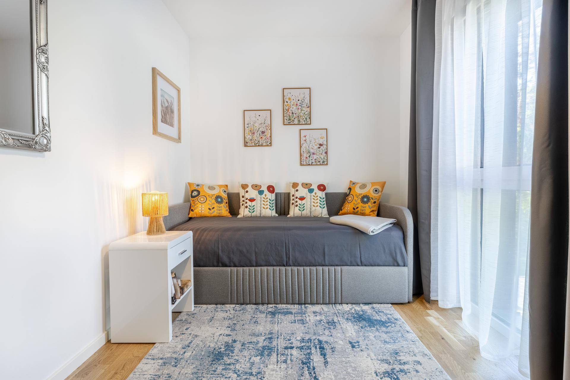 Helles Zimmer mit Tagesbett, Nachttisch und dekorativen Kissen, ideal als Gästezimmer.