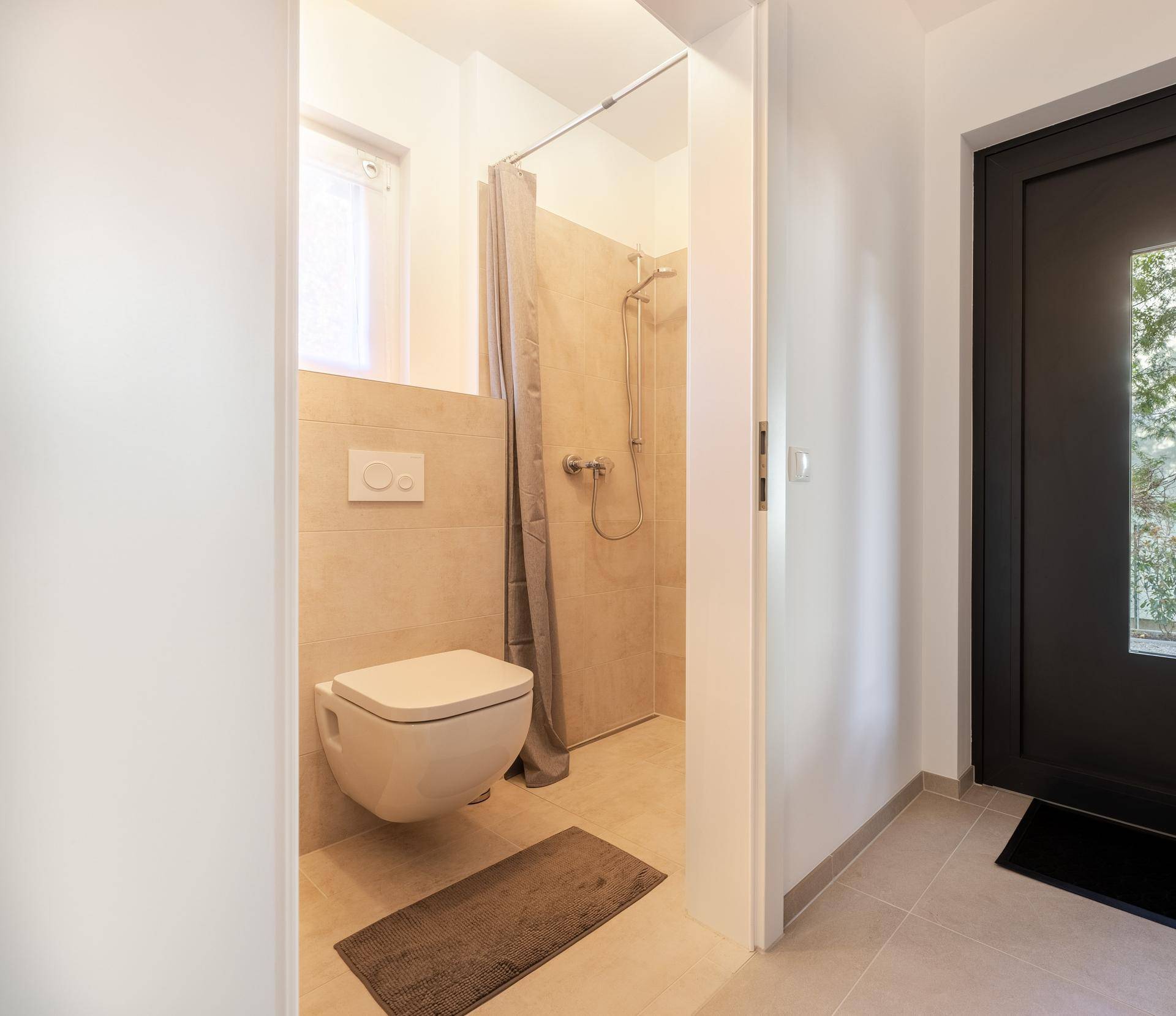 Kleines Badezimmer mit Dusche, WC und Fenster im Eingangsbereich.