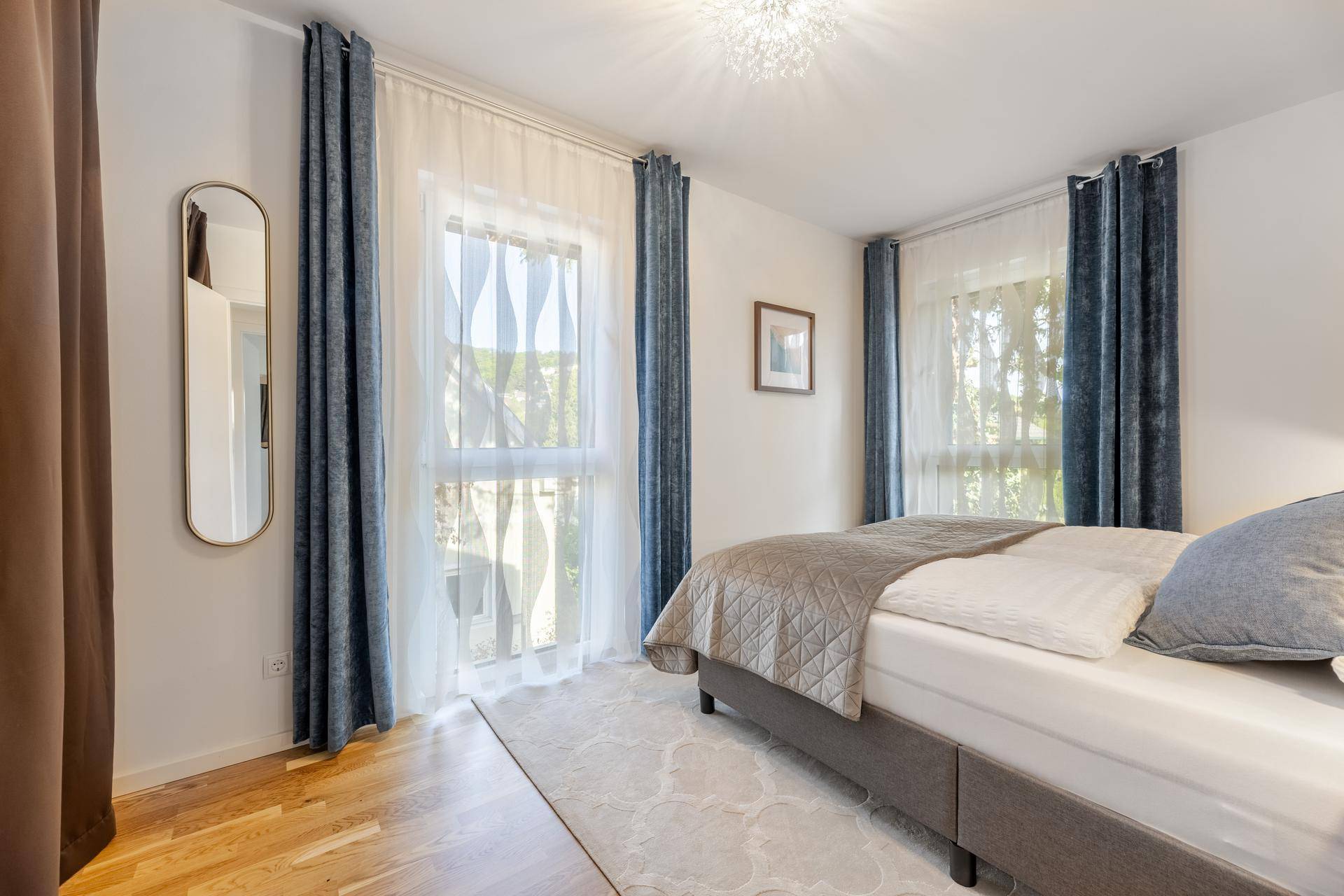 Helles Schlafzimmer mit großem Fenster, Vorhängen und Blick ins Grüne.