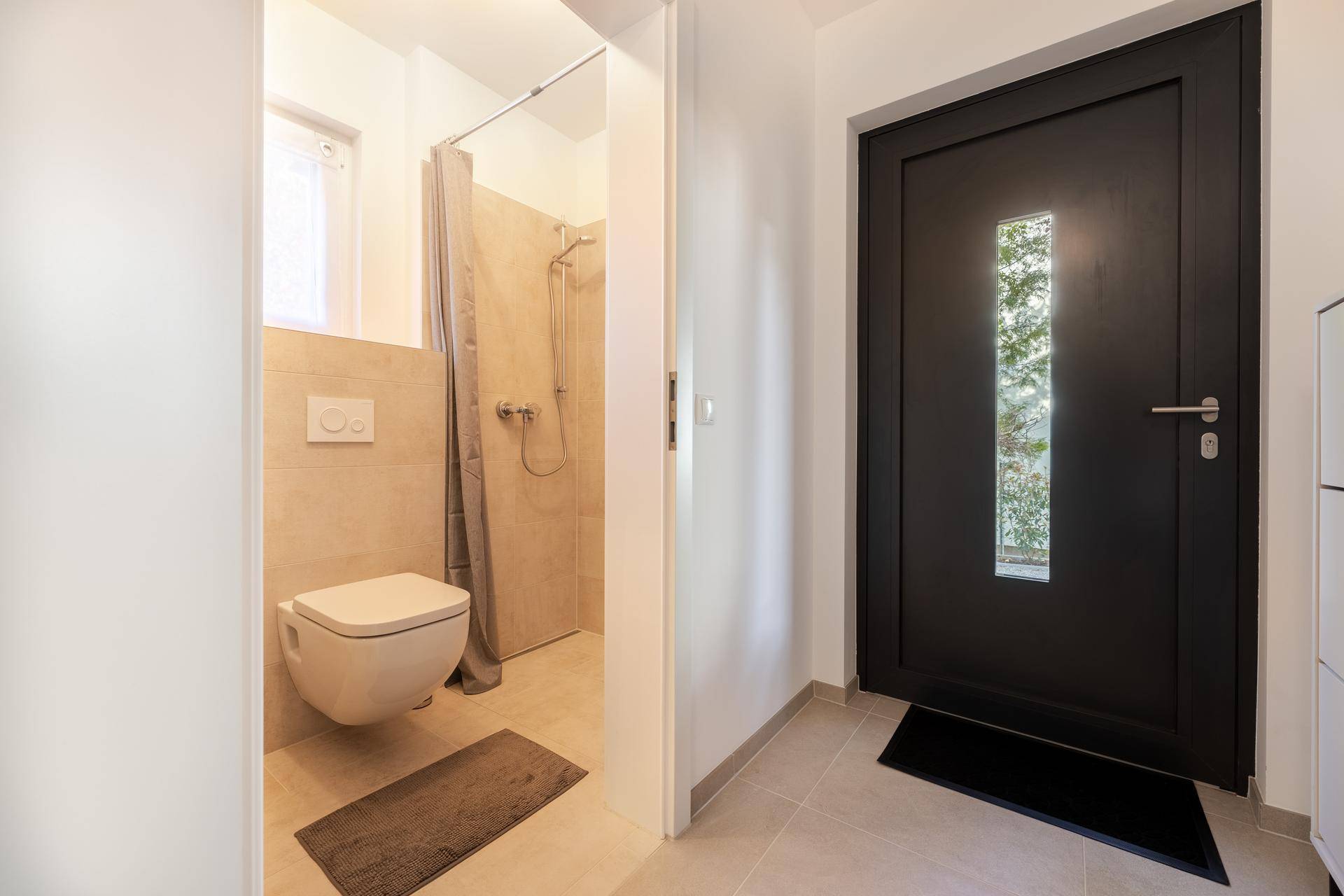 Kleines Badezimmer mit Dusche und wandhängendem WC, direkt neben dem Eingangsbereich.