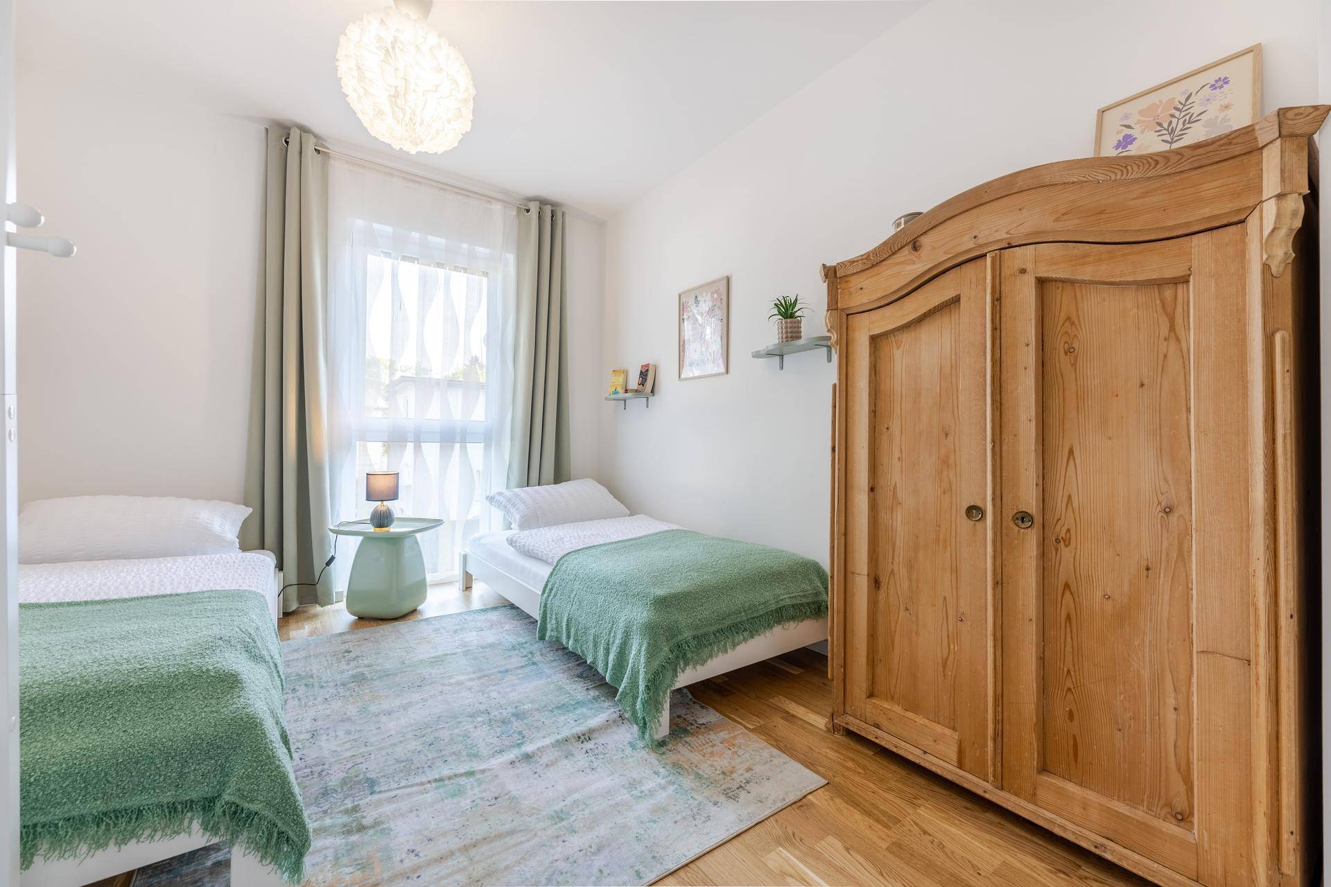 Helles Kinder- oder Gästezimmer mit zwei Einzelbetten, Holzboden und antikem Schrank.