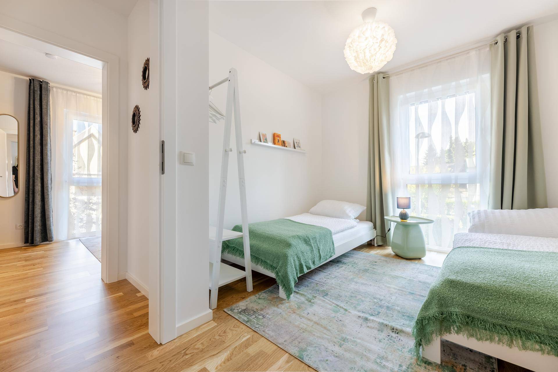 Freundliches Kinderzimmer mit Einzelbetten, Holzboden und viel Tageslicht durch das Fenster.