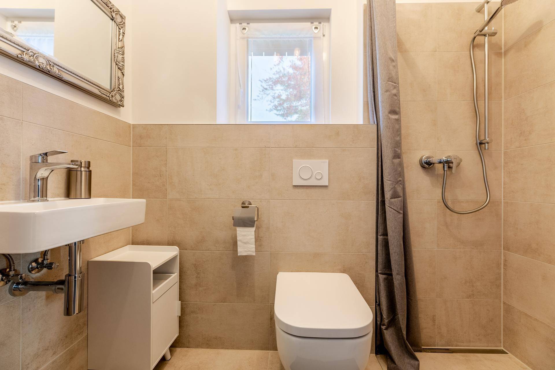 Modernes Badezimmer mit beigen Fliesen, Dusche, Waschbecken und Fenster für Tageslicht.
