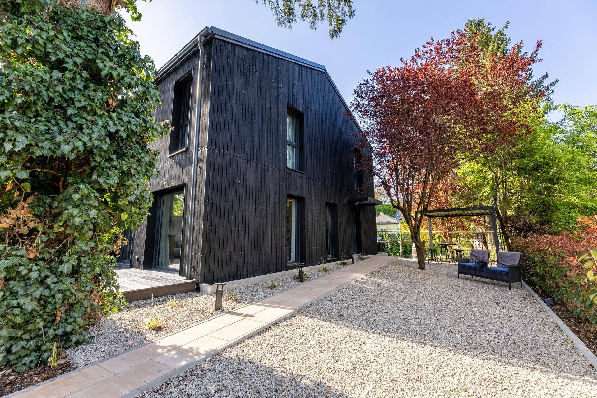Modernes schwarzes Haus mit Kiesweg und üppiger Begrünung im Gartenbereich.