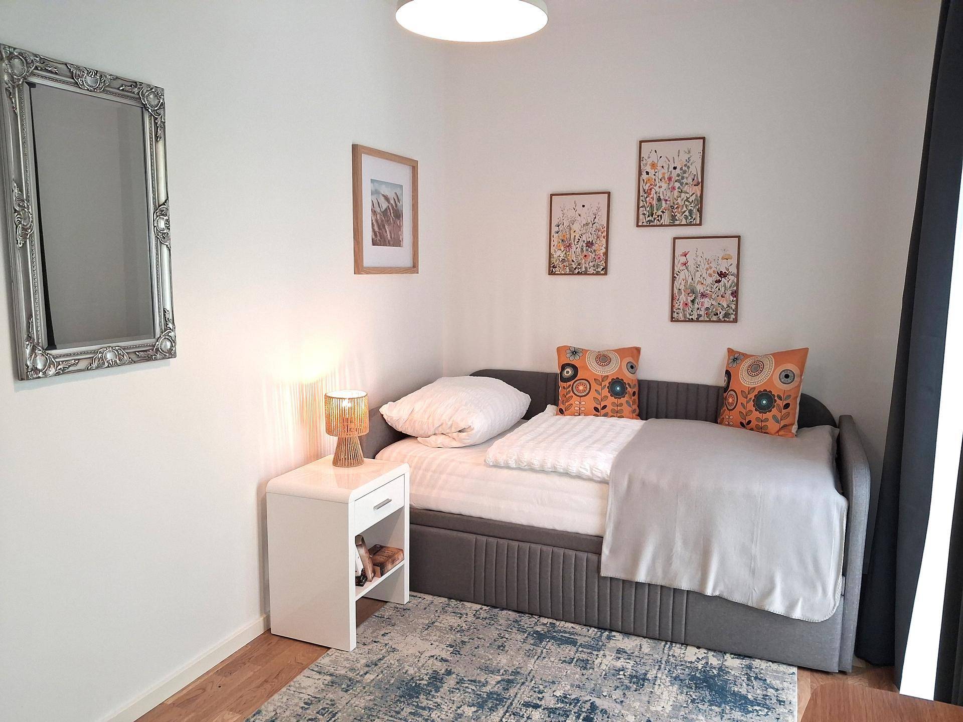 Flexibles Zimmer mit ausziehbarem Tagesbett, Teppich und hellem Fenster.
