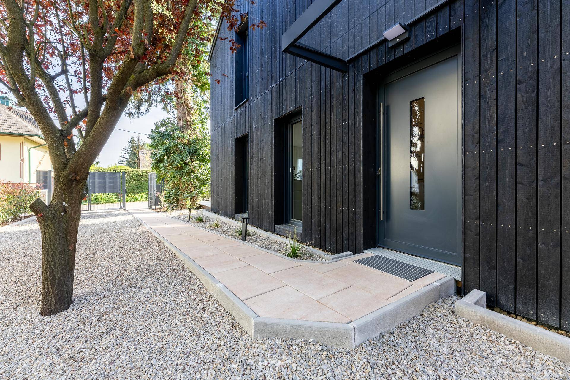 Moderne Hausfassade aus dunklem Holz mit Eingangsbereich und Kiesweg.