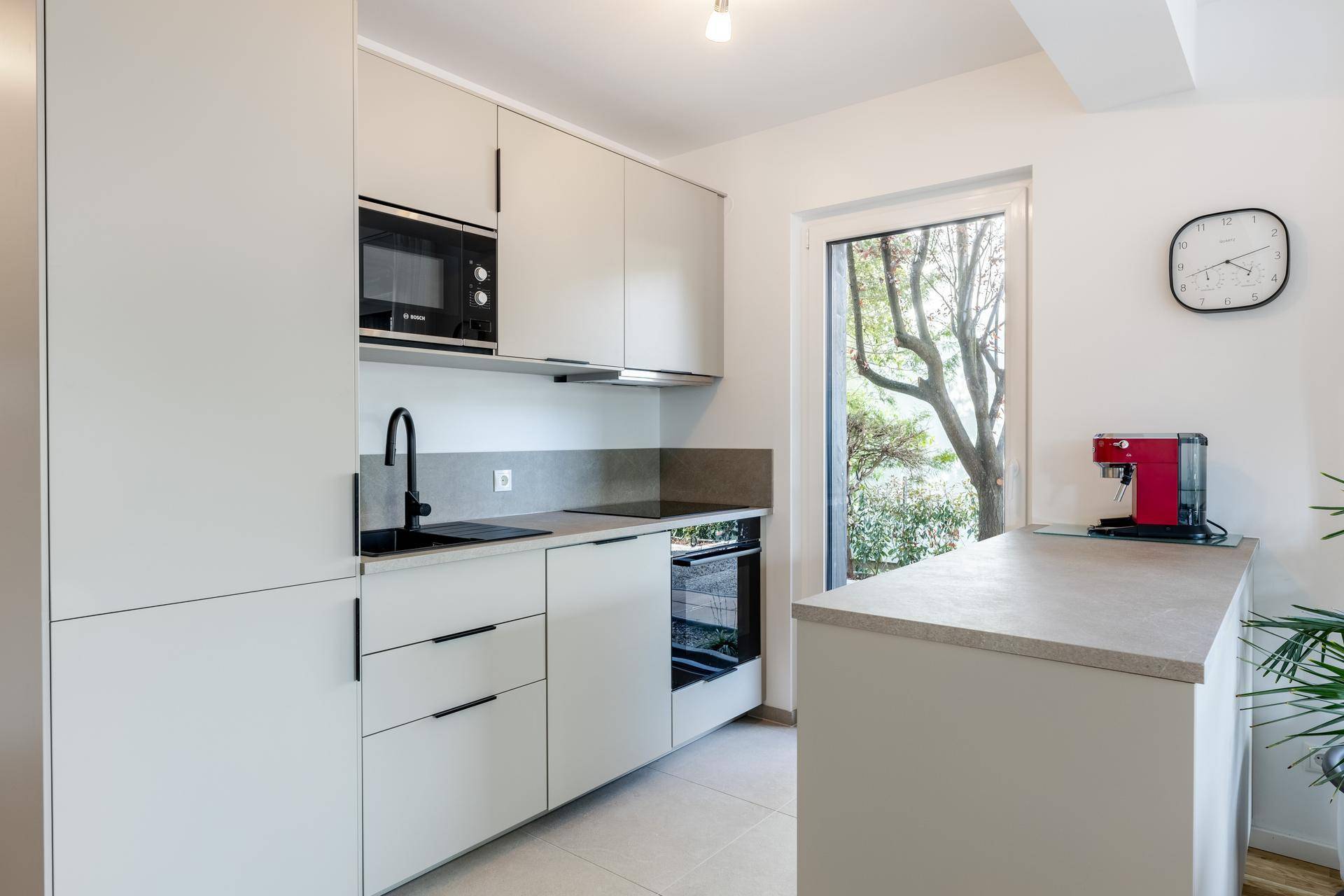Moderne Einbauküche mit hellen Schränken, integrierten Geräten und Fenster mit Grünblick.