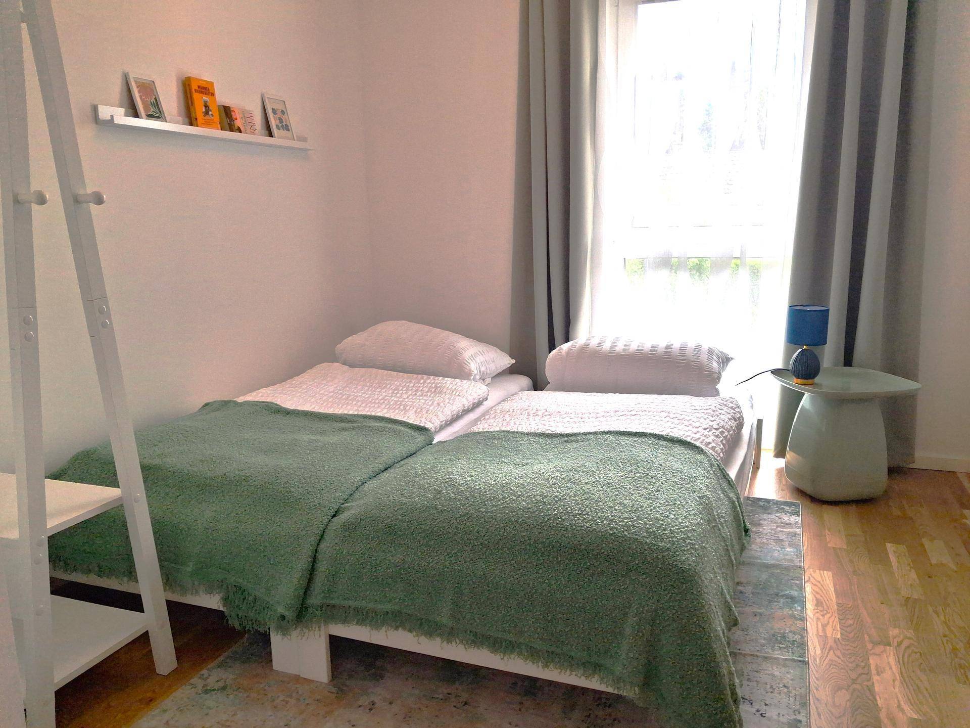 Gemütliches Kinderzimmer mit zwei Betten, Teppich und hellem Fenster für natürliche Beleuchtung.