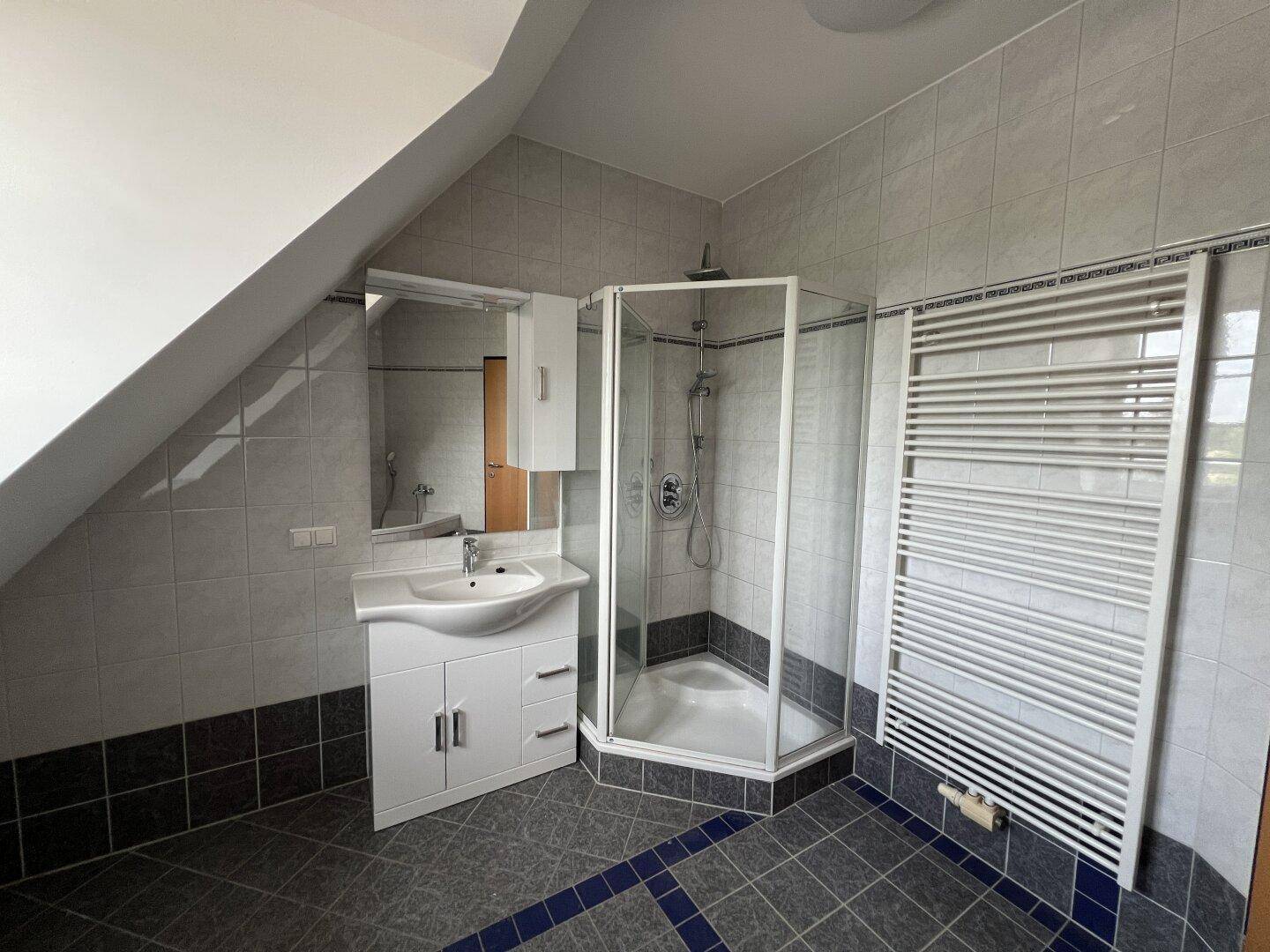 Duschkabine und Waschtisch im Badezimmer mit Fliesenboden und beheiztem Handtuchhalter.