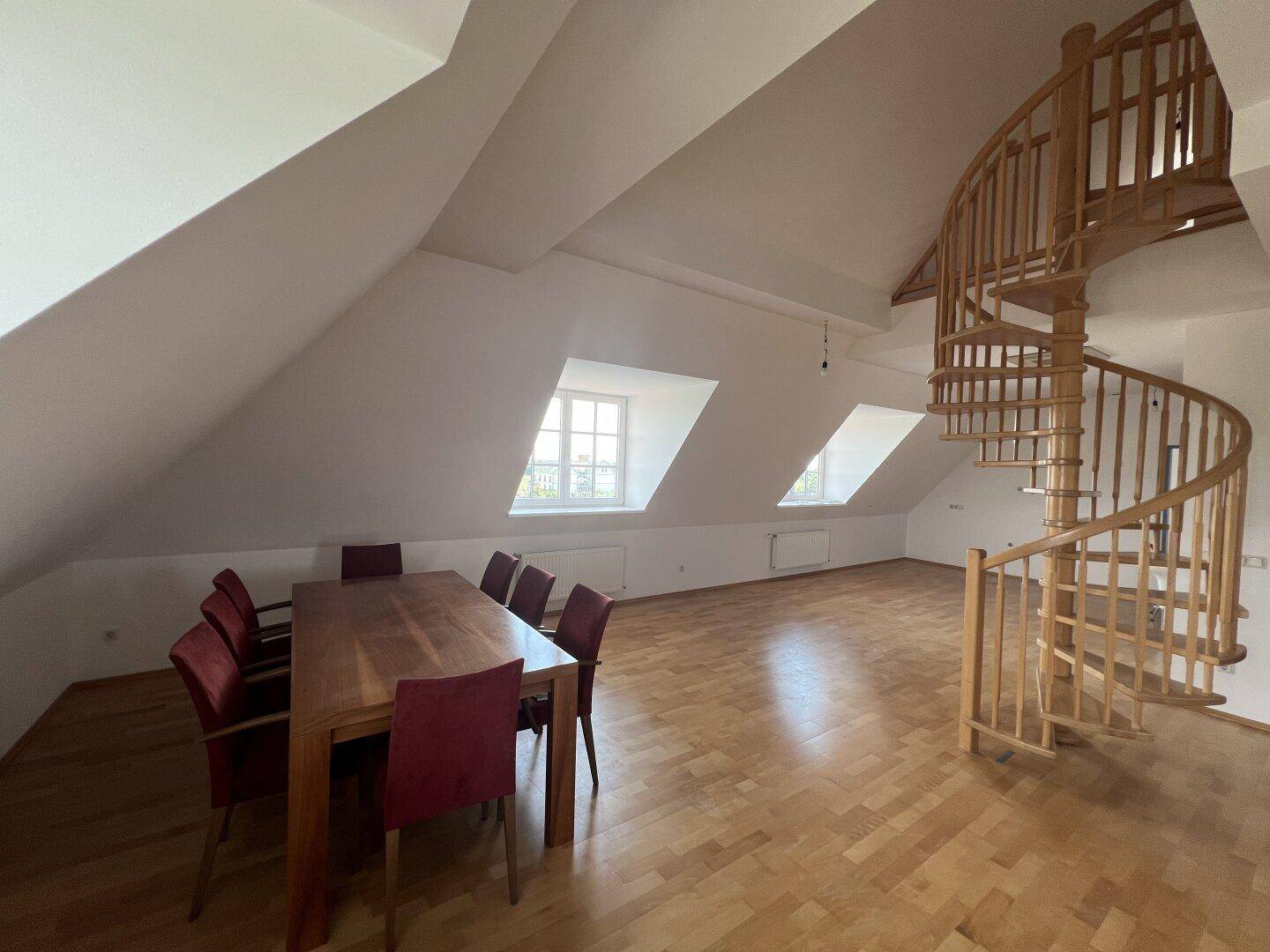 Geräumiger offener Wohn- und Essbereich im Dachgeschoss mit Holzwendeltreppe und schrägen Decken.