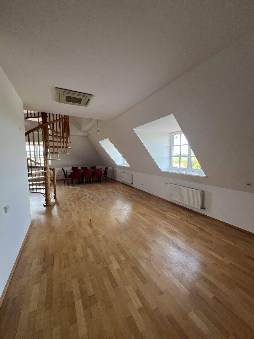 Heller Wohn- und Essbereich mit Holzwendeltreppe, Klimaanlage und Blick ins Grüne.