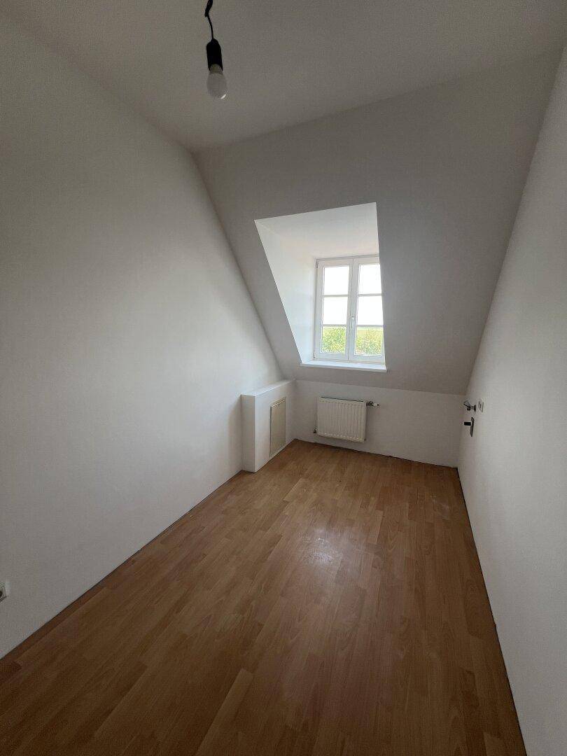 Leeres Zimmer im Dachgeschoss mit Holzfußboden, Dachschräge und Fenster.