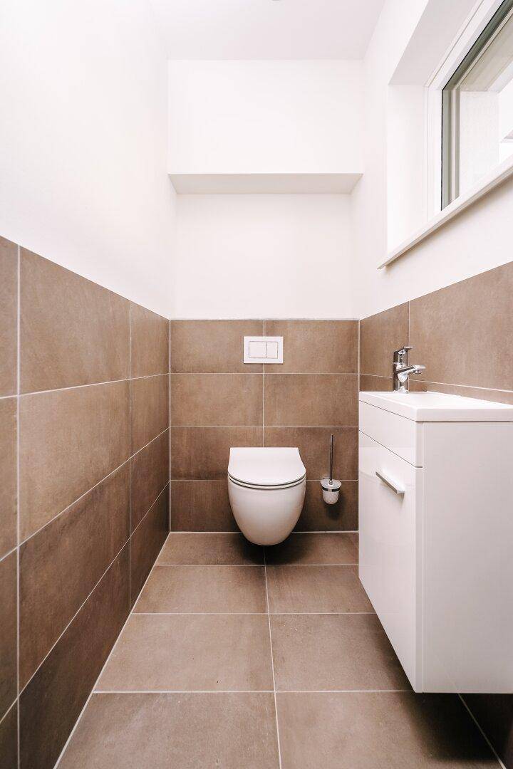 Modernes Gäste-WC mit braunen Fliesen, wandhängendem WC und Fenster.