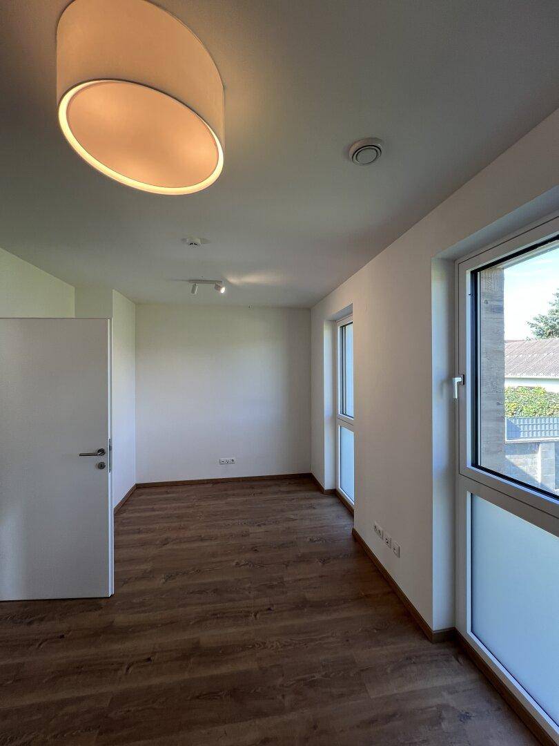 Helles Zimmer mit großen Fenstern und Laminatboden, ideal als Schlafzimmer.