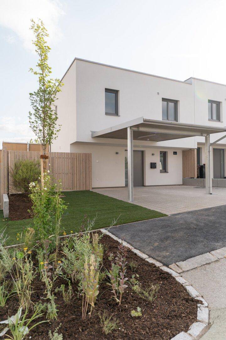 Modernes Reihenhaus mit Carport, kleinem Vorgarten und Holzzaun in einer Wohnsiedlung.