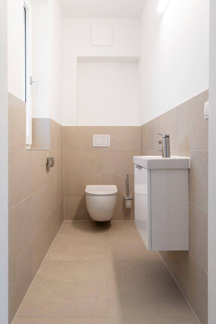 Modernes Gäste-WC mit beigefarbenen Fliesen, wandhängendem WC und einem einzelnen Waschbecken.