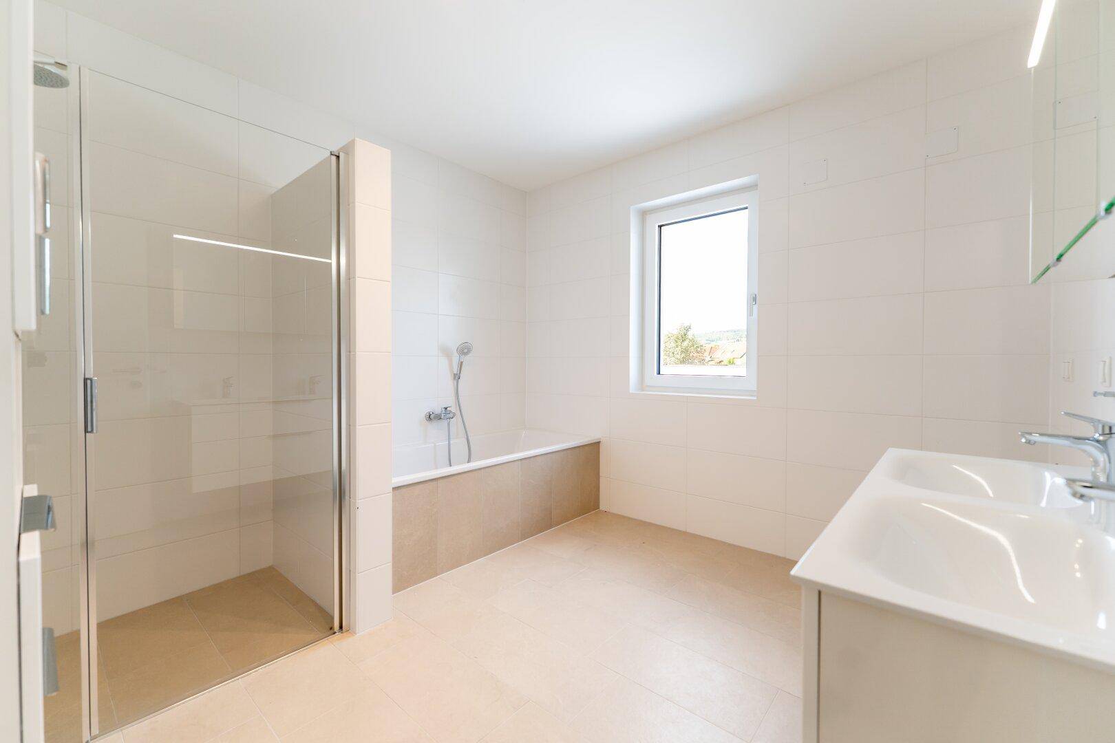 Helles Badezimmer mit begehbarer Dusche, Badewanne, Doppelwaschbecken und Fenster.