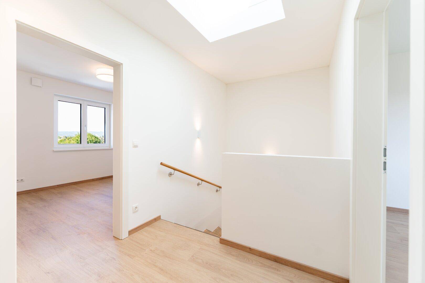 Heller Flur im Obergeschoss mit Laminatboden, Holzgeländer und einem Oberlicht für natürliches Licht.