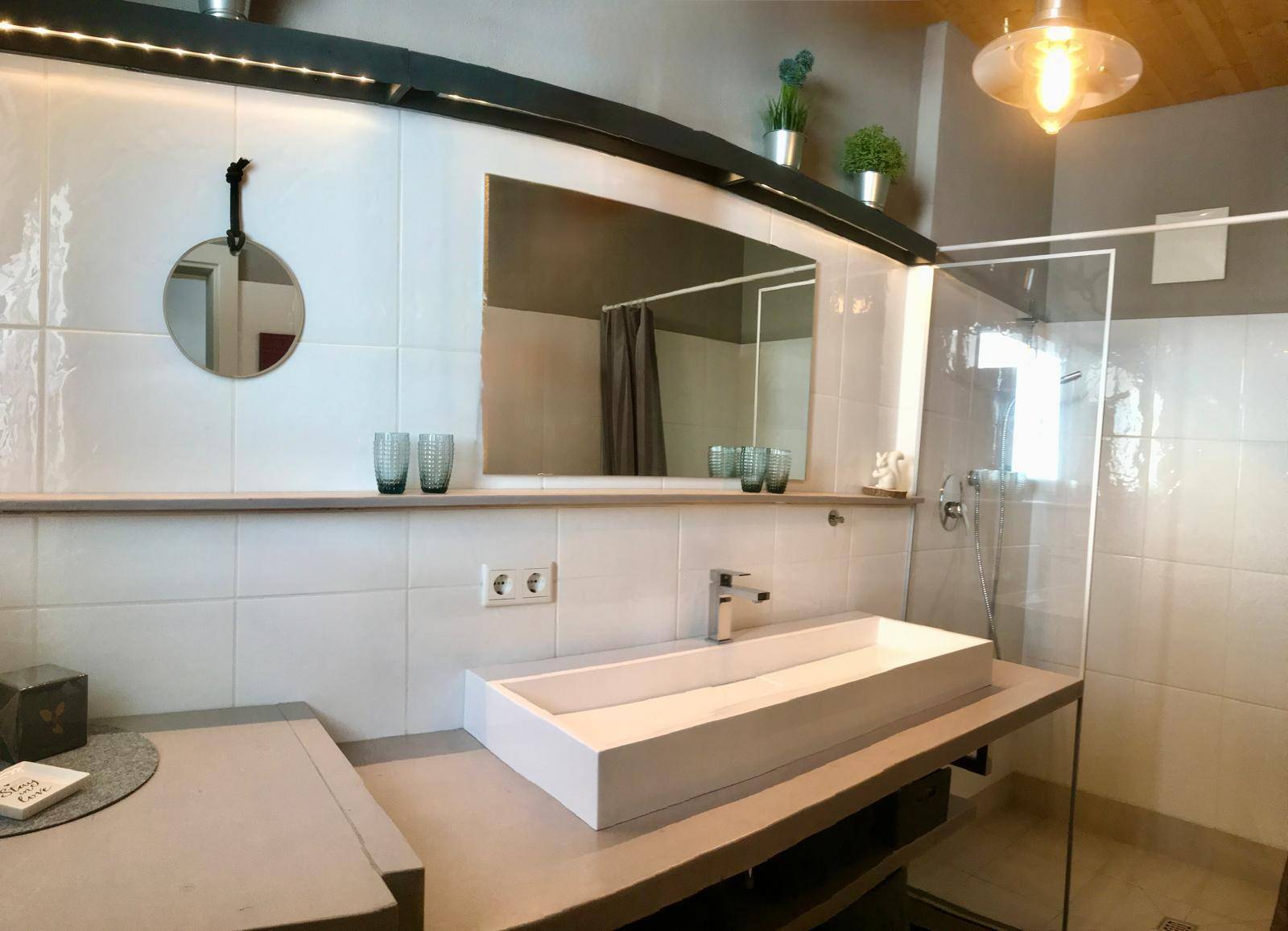 Helles Badezimmer mit modernem Waschbecken, großer Spiegelfläche und Duschbereich.