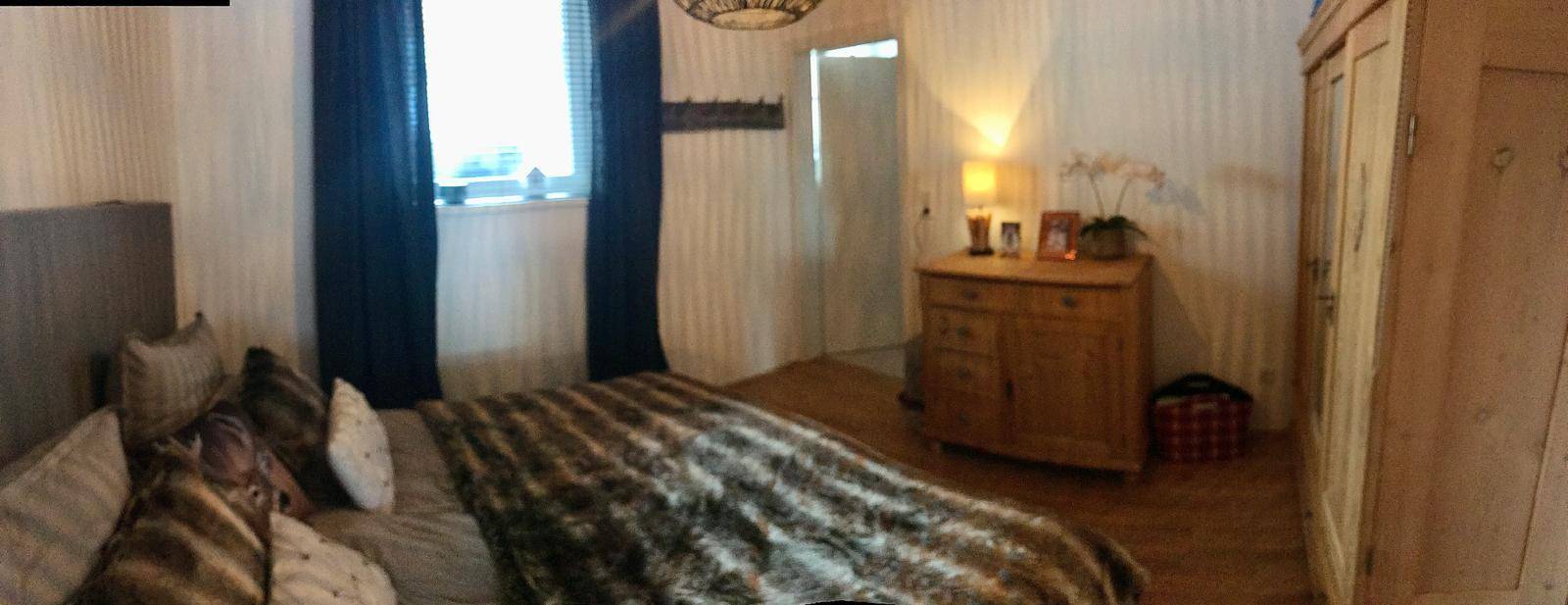 Gemütliches Schlafzimmer mit Holzboden, großem Kleiderschrank und Fenster mit blauen Vorhängen.